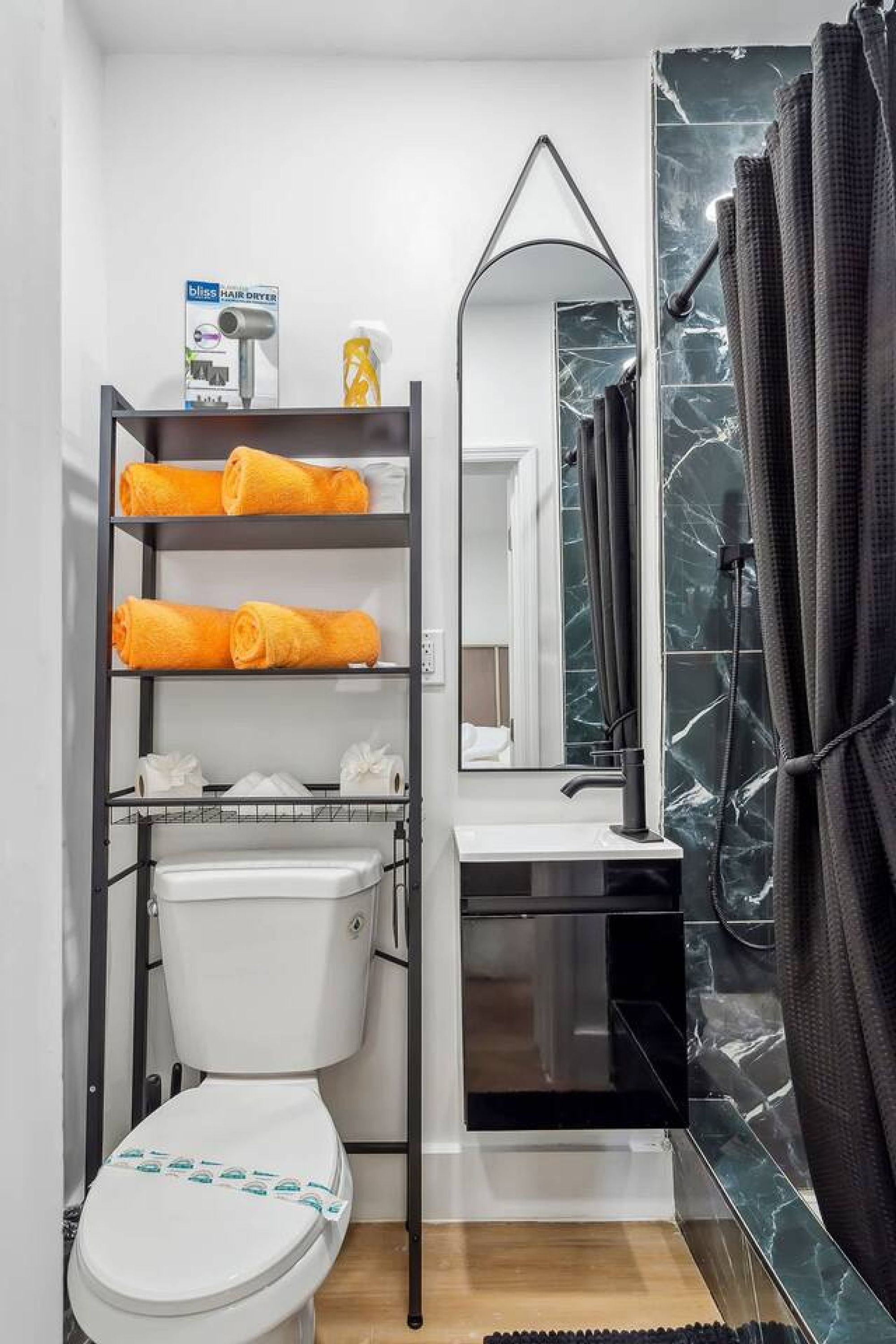 Baño compacto con inodoro blanco, lavabo negro, espejo y repisa con toallas.