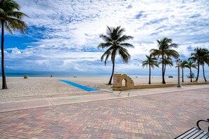 A beachside walkway with palm trees, a clear sky, and a view of the ocean.