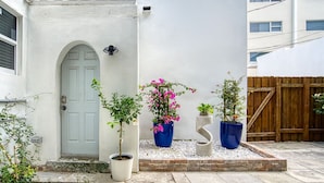 Un bâtiment blanc avec une porte grise, des plantes en pot et une clôture en bois.