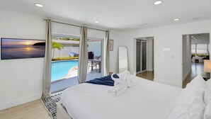 Habitación de hotel moderna con una cama grande, un televisor montado en la pared y vistas a una piscina exterior.