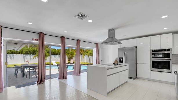 Una cocina moderna con gabinetes blancos, un refrigerador de acero inoxidable y una isla con pileta.