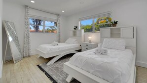 Un dormitorio moderno con dos camas, un ventanal grande y un espejo sobre las camas.