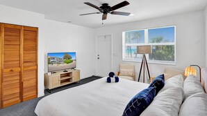 A modern bedroom with a bed, a ceiling fan, a TV, a wardrobe, and a window with blinds.