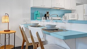 A modern kitchen with white cabinets, a blue countertop, and a dining area with white chairs and a small table.