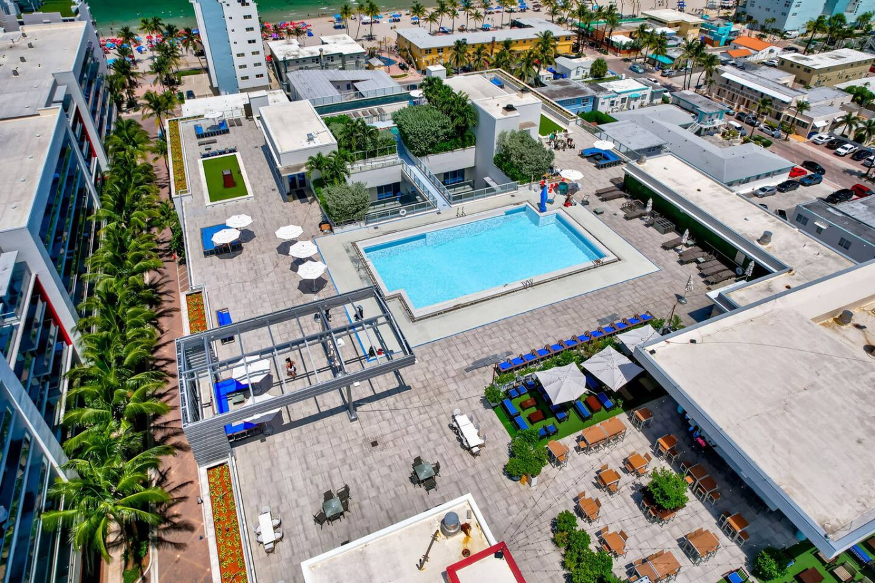 An aerial view of a hotel with a swimming pool, outdoor seating areas, and a rooftop bar.