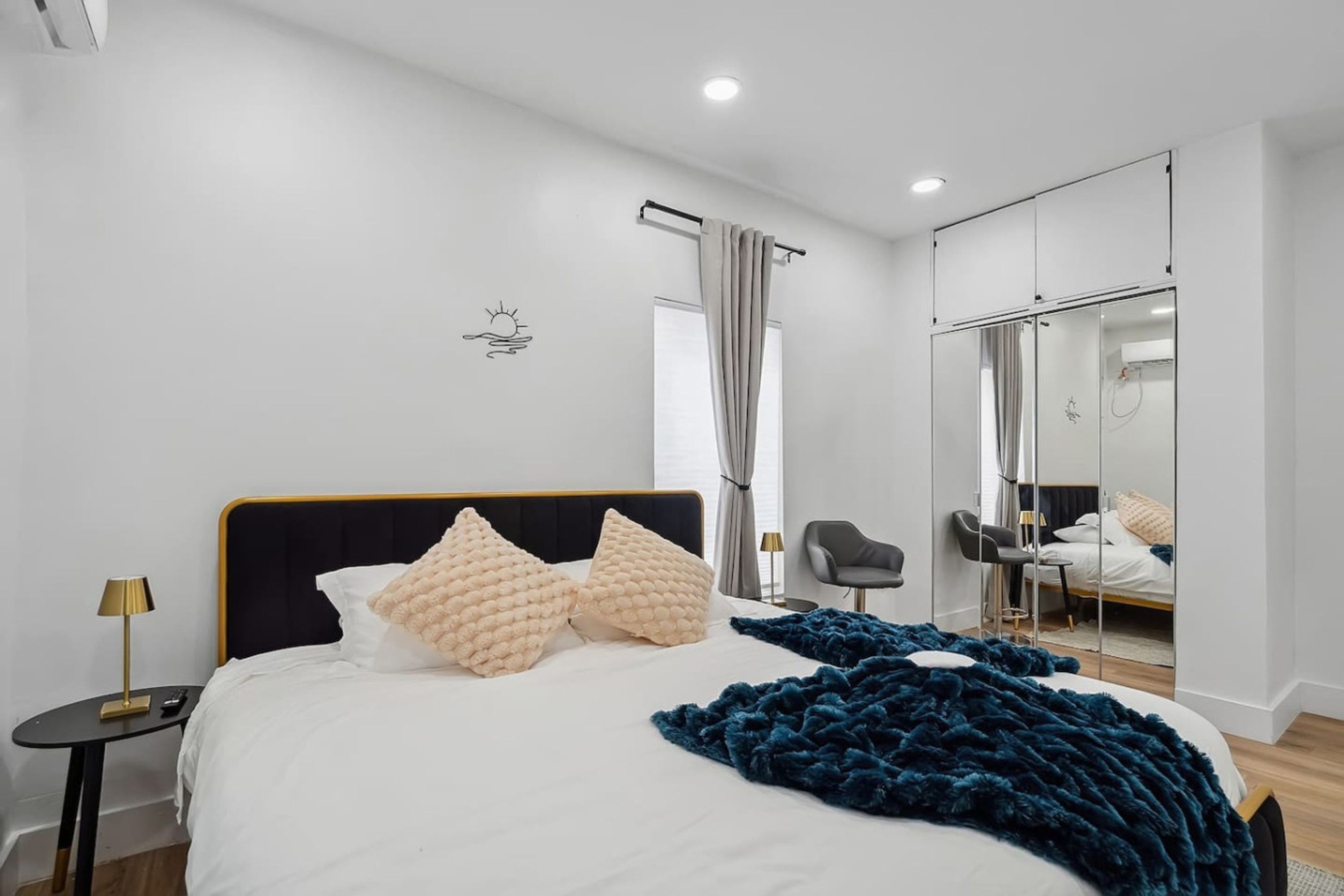 A modern bedroom with a large bed, a bedside table with a lamp, a chair, a mirror, and a view of the outside.