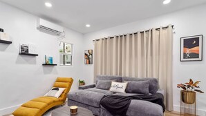 Ein modernes Wohnzimmer mit einer Couch, einem gelben Sessel, einem runden Couchtisch und einem großen Fenster mit Vorhängen.