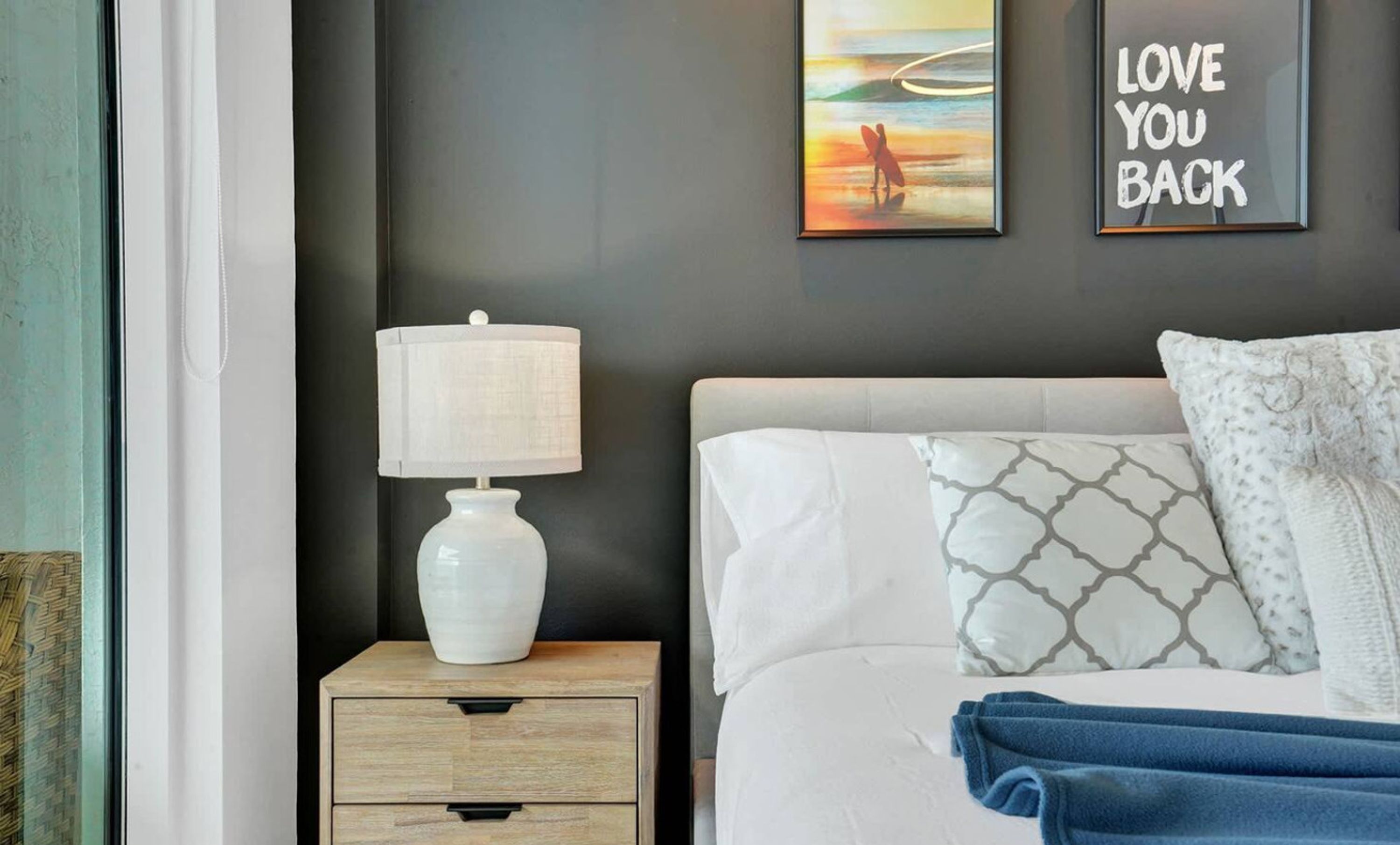 A bedroom with a bed, a nightstand with a lamp, and two wall art pieces.
