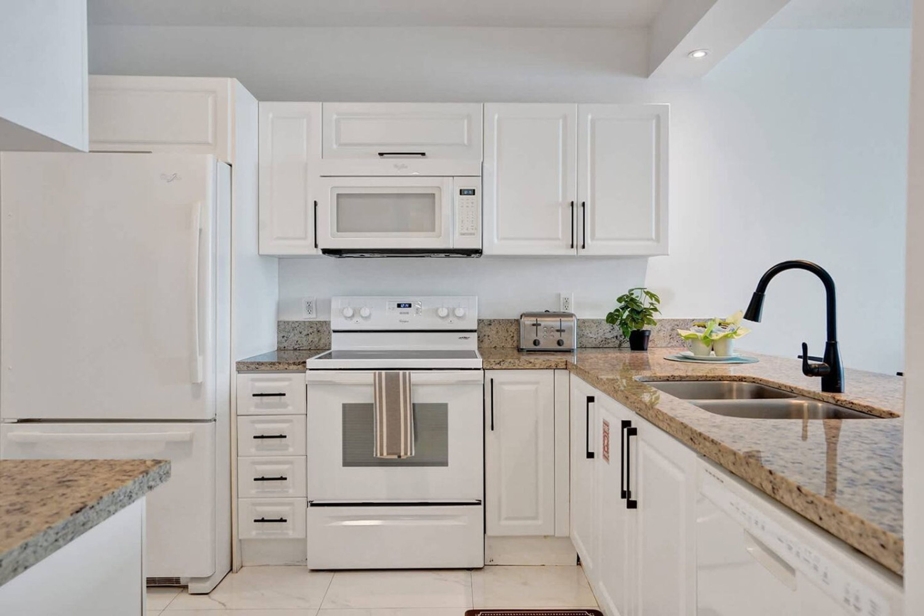 A modern kitchen with white cabinetry, a built-in microwave, a stove, and a sink.