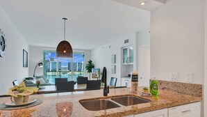 Cocina moderna con encimeras de granito, pileta doble y vista panorámica de la ciudad a través de amplias ventanas.