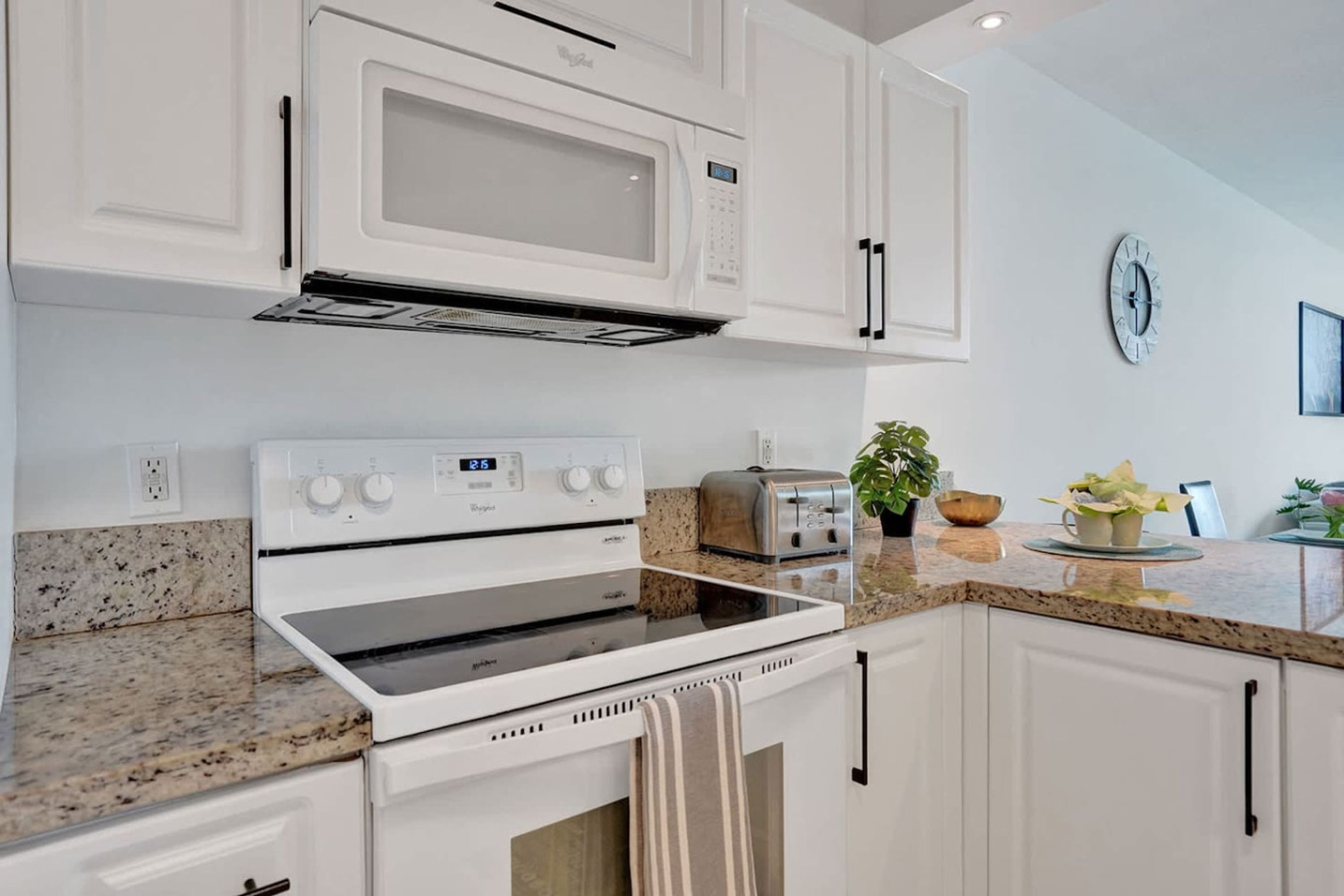 A modern kitchen with white cabinetry, a built-in microwave, a stove, and a toaster.