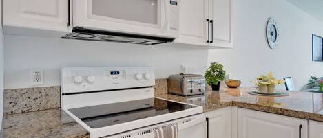 A modern kitchen with white cabinetry, a built-in microwave, a stove, and a toaster.