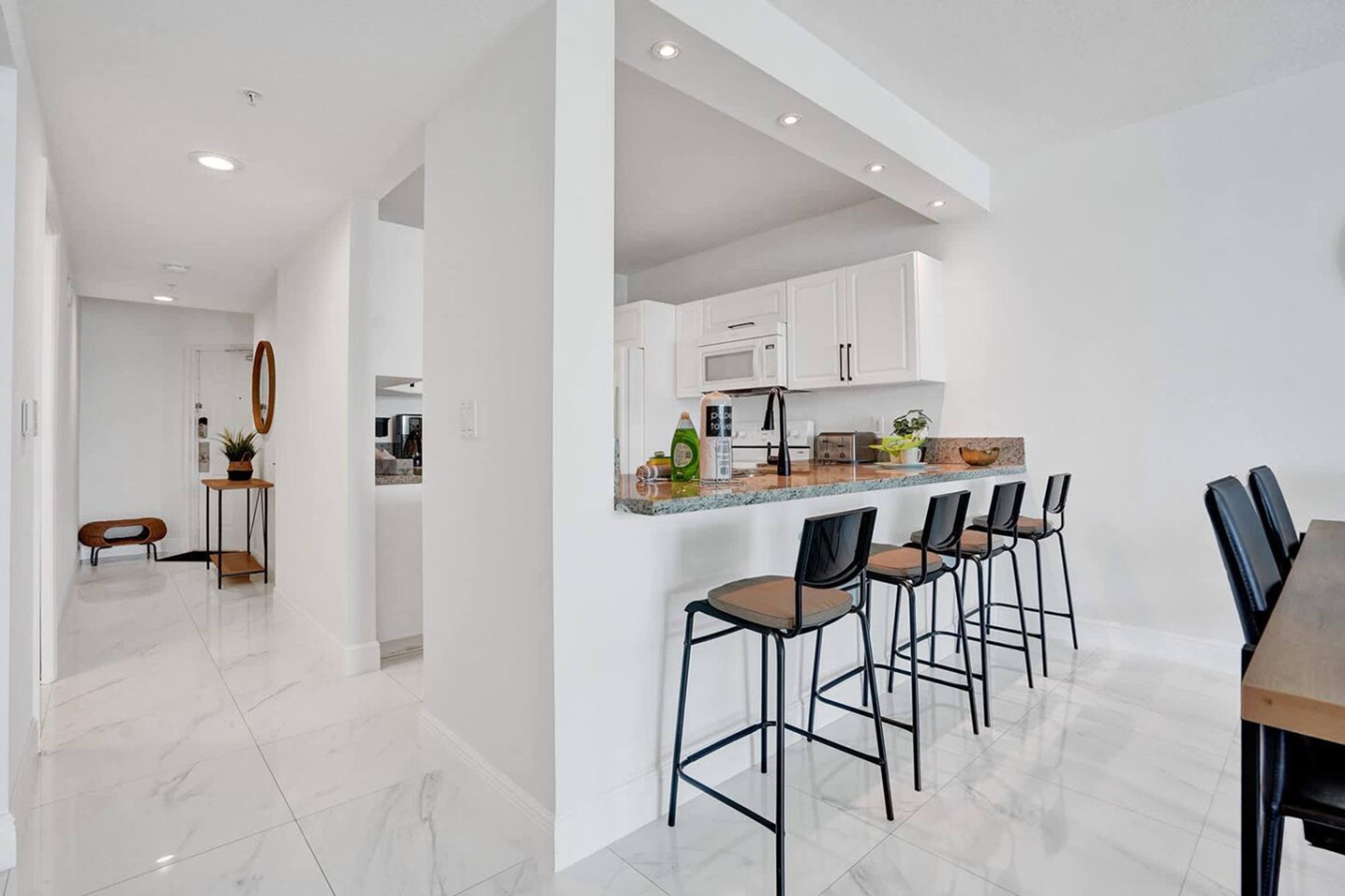 A modern kitchen with white cabinets, a granite countertop, and bar stools.