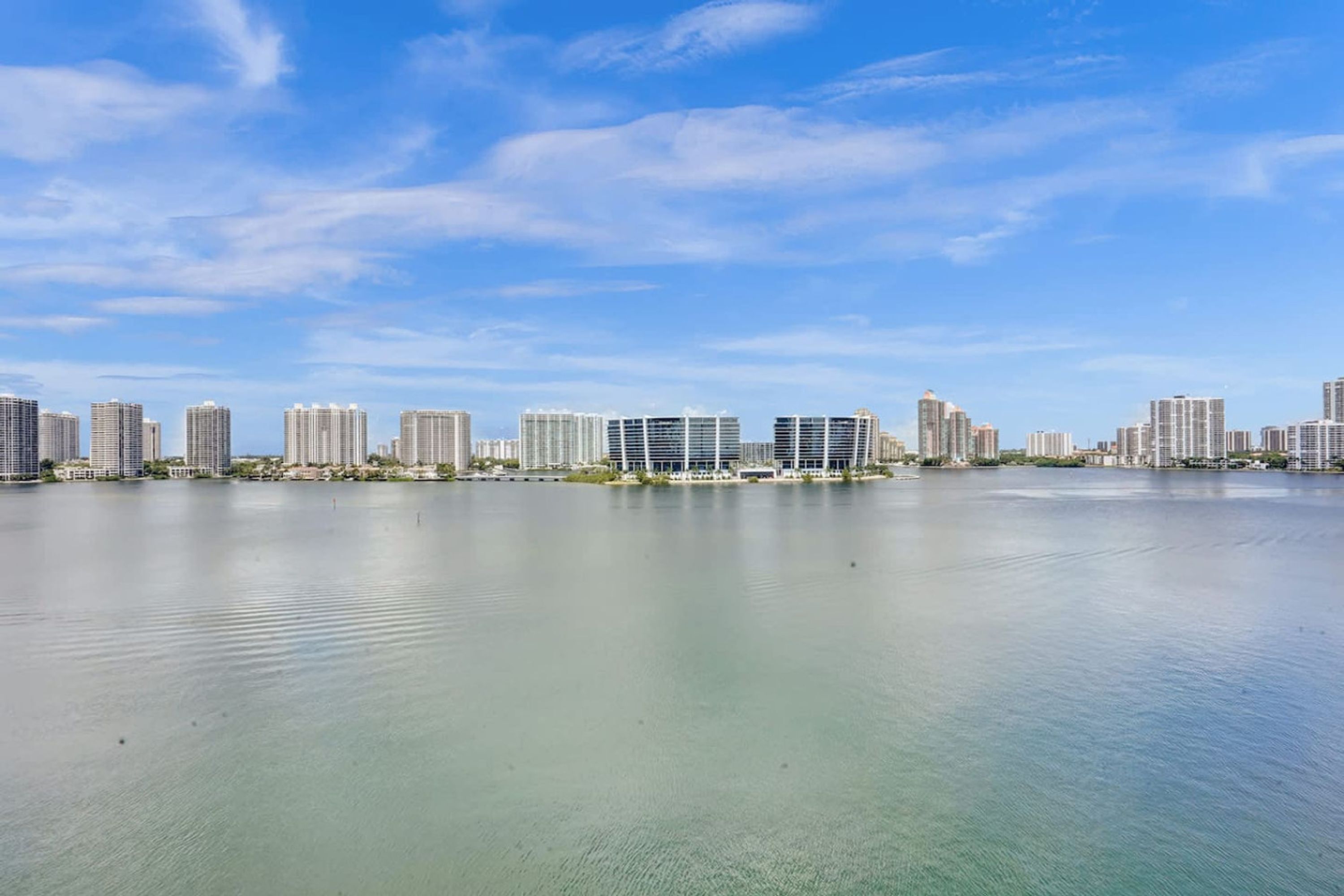 A waterfront cityscape with high-rise buildings and a calm body of water.