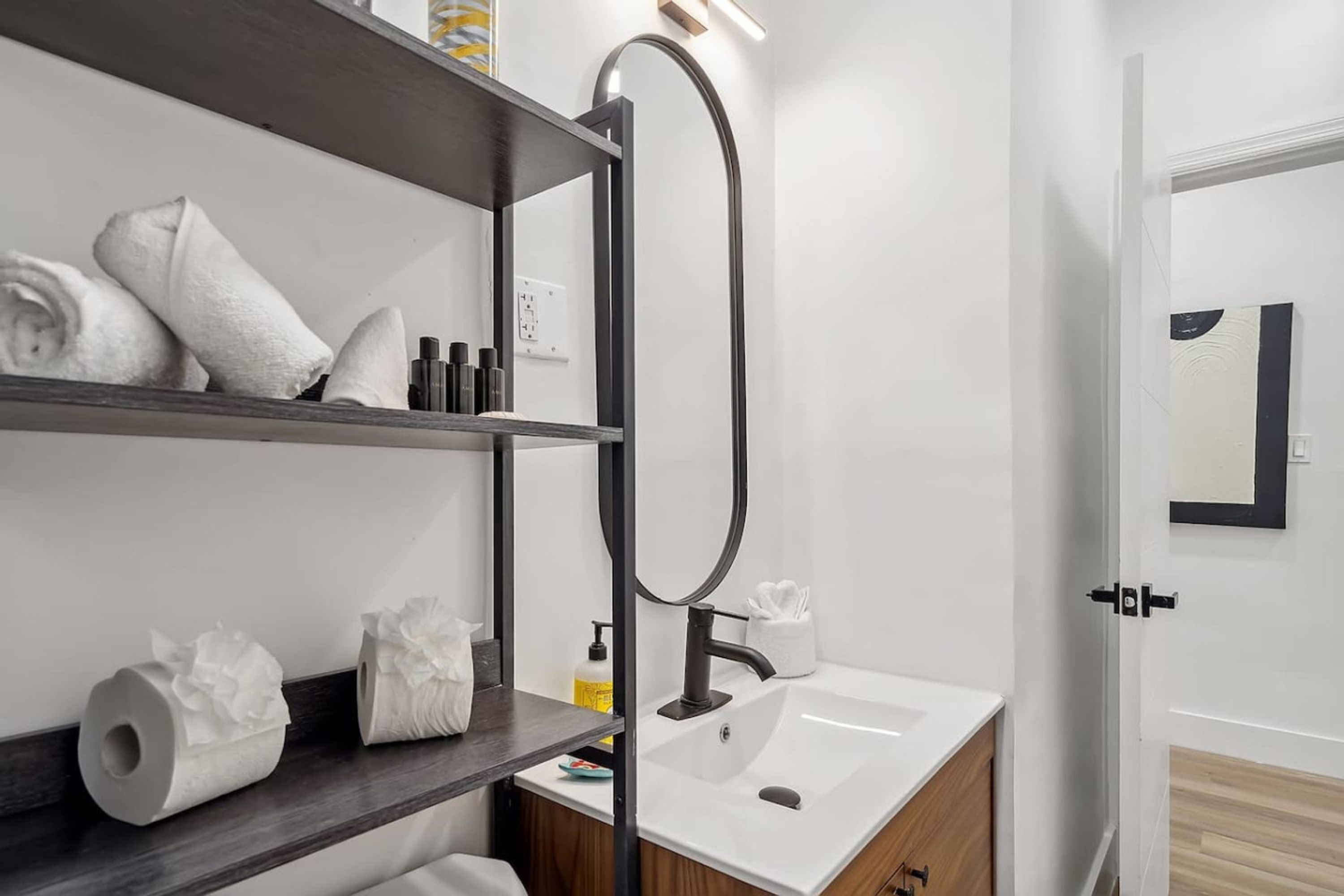 A modern bathroom with a white sink, dark wooden shelves, and a large mirror.