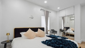 Une chambre à coucher moderne avec un grand lit, une table de chevet avec une lampe, une chaise et un miroir.