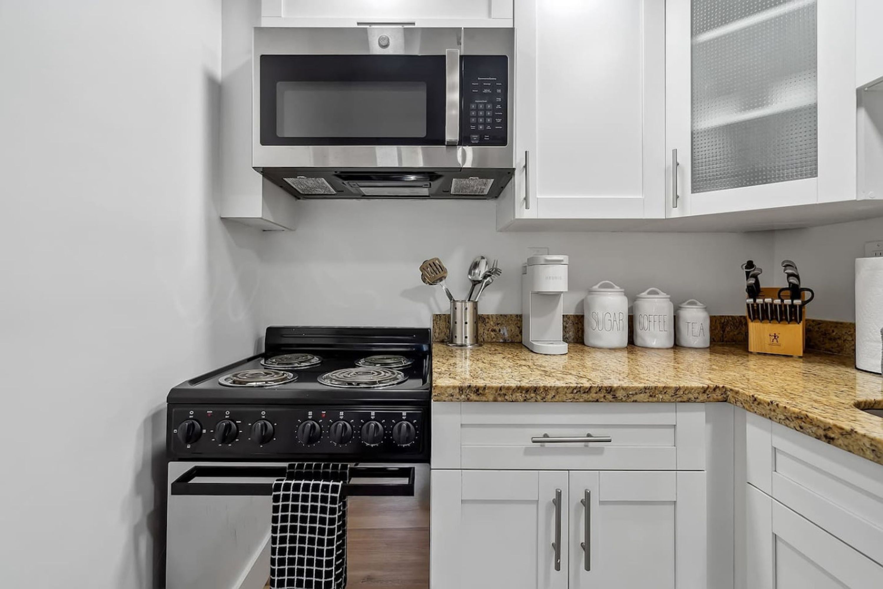 A modern kitchen with white cabinets, a black stove, a microwave, and a granite countertop.