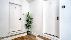 Un couloir avec deux portes blanches, numérotées 1 et 2, une plante en pot et un paillasson.