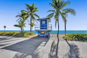 A lifeguard tower with a blue and yellow color scheme, surrounded by palm trees and a clear view of the ocean. - Waves on Desoto Deluxe Studio 4 (Hollywood)