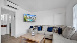 Een moderne woonkamer met een grijze bank, een houten salontafel en een flatscreen televisie aan de muur.