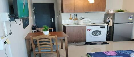 A compact kitchen with a washing machine, a refrigerator, wooden cabinets, and a dining area with a table and chairs.