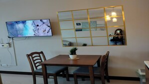 Zona pranzo con tavolo e sedie in legno, TV a schermo piatto montata a parete e uno specchio decorativo.