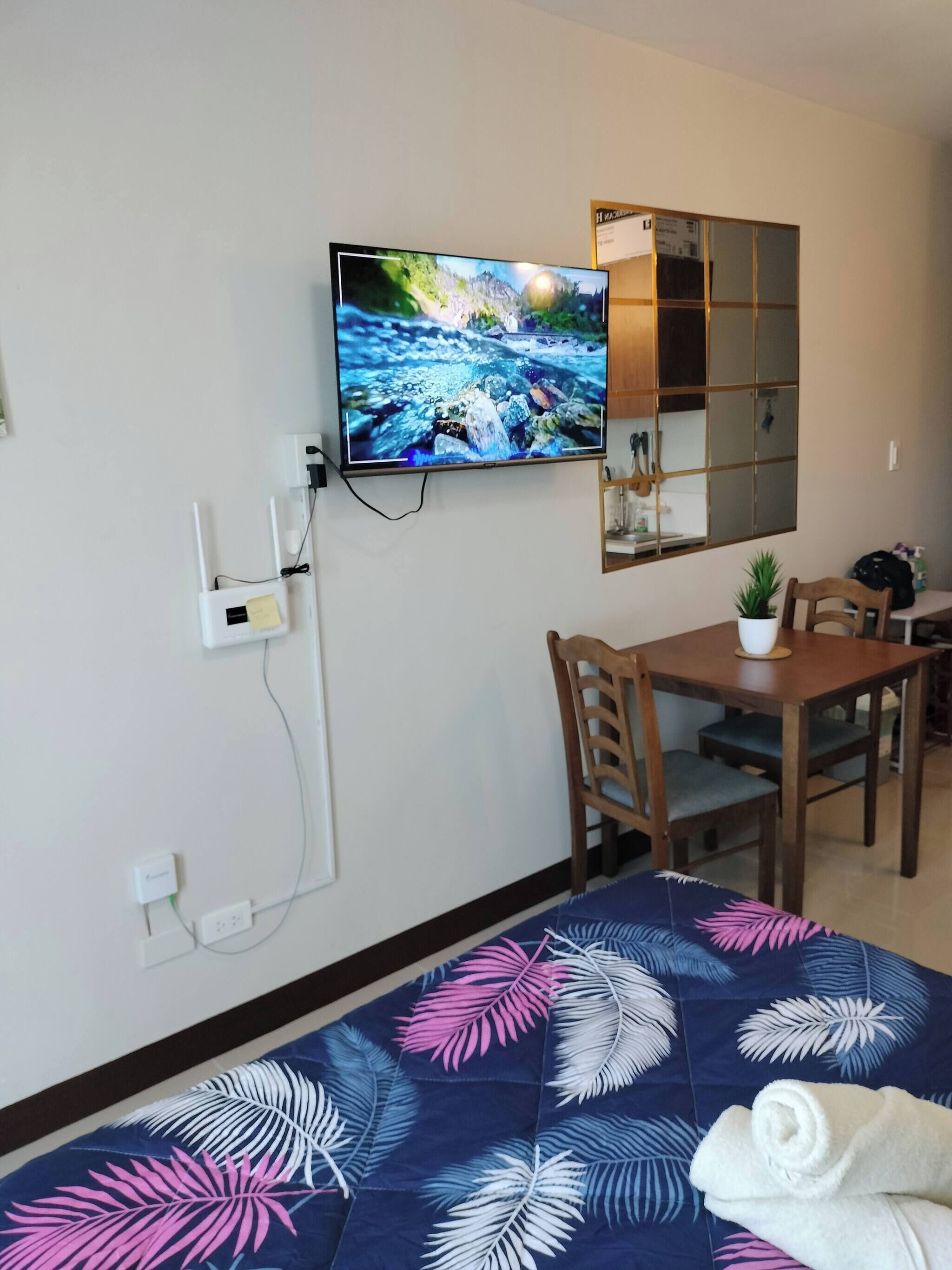 Une chambre d’hôtel avec un lit, un téléviseur fixé au mur, une petite table avec des chaises et un miroir au-dessus de la table.