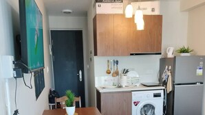 Una cucina compatta con mobili in legno, forno a microonde, lavatrice e frigorifero.