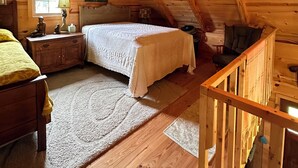 A cozy attic bedroom with a wooden ceiling, a bed, a nightstand, a dresser, and a chair.
