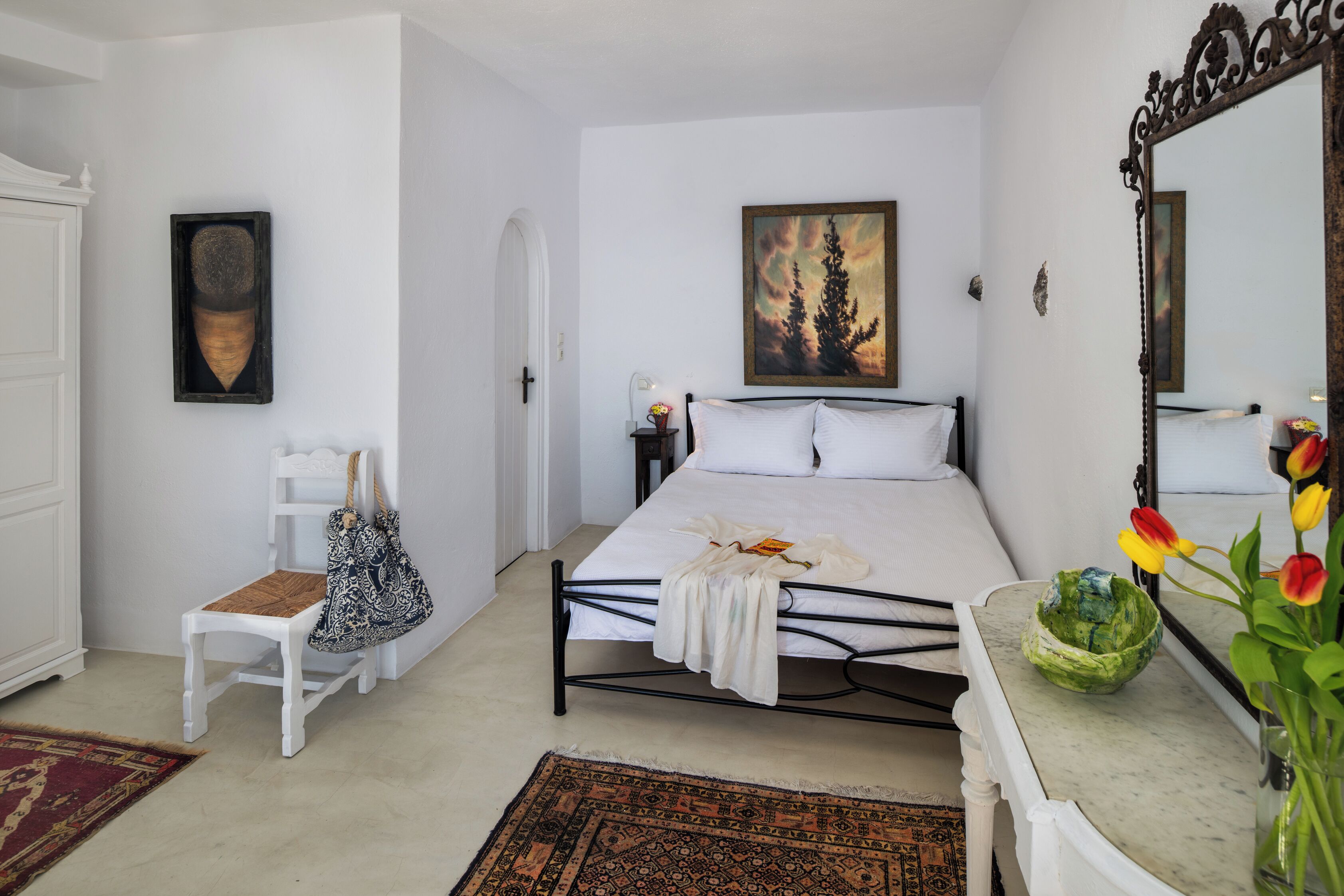A bedroom with a bed, a chair, a dresser, a mirror, and a painting on the wall.