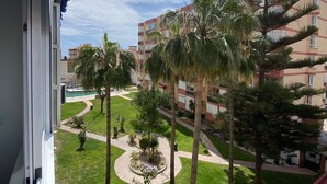 A view from a balcony overlooking a landscaped courtyard with palm trees, a circular flower bed, and a pool.