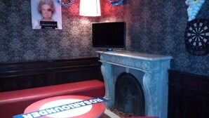 A room with a television on a stand, a dartboard, and a red couch. - Che Pampa´s Hostel (Rosario)