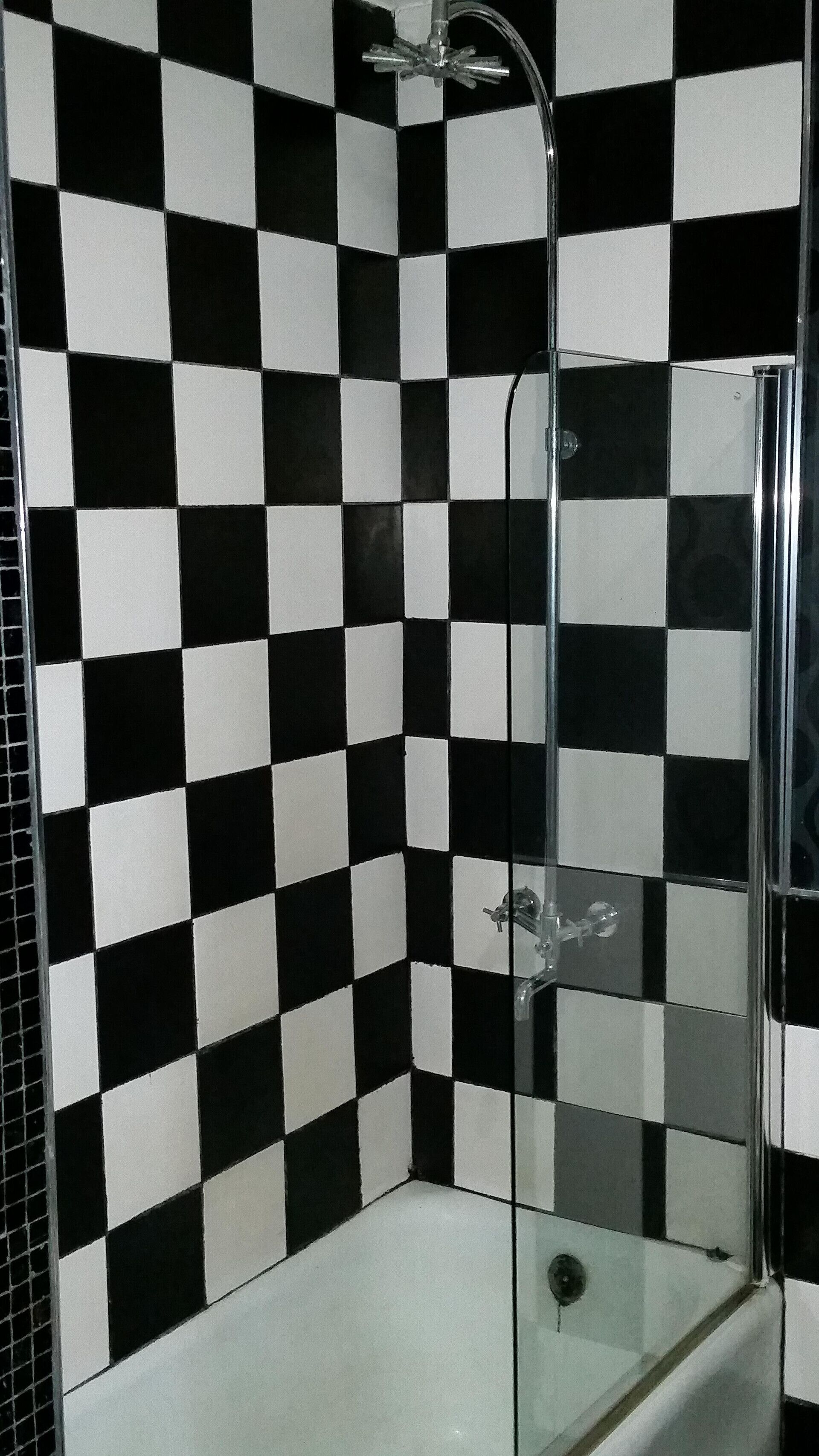 A shower with a glass door and a black and white checkered wall.