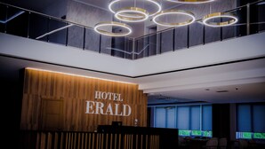 En moderne hotellobby med en receptionsdisk, en trappe og udsigt til det fri gennem store vinduer.