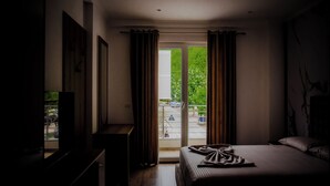 Et hotelværelse med en seng, et fjernsyn og udsigt over et grønt udendørsområde gennem en glasdør.