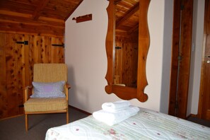Une pièce aux murs lambrissés, contenant un lit, une chaise et un miroir.