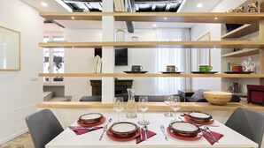 A dining area with a white table set for four, surrounded by wooden shelves with various items.