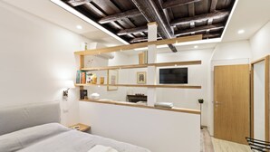 A modern bedroom with a bed, bedside table, and a wooden shelf with books and decorative items.