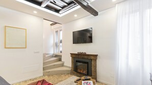 A living room with a fireplace, a TV mounted on the wall, and a staircase leading to another level.