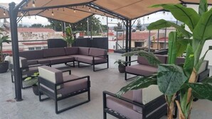 An outdoor seating area with cushioned sofas and tables, surrounded by potted plants.