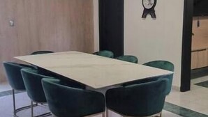 A conference room with a long table and six chairs, a clock on the wall, and a door in the background.