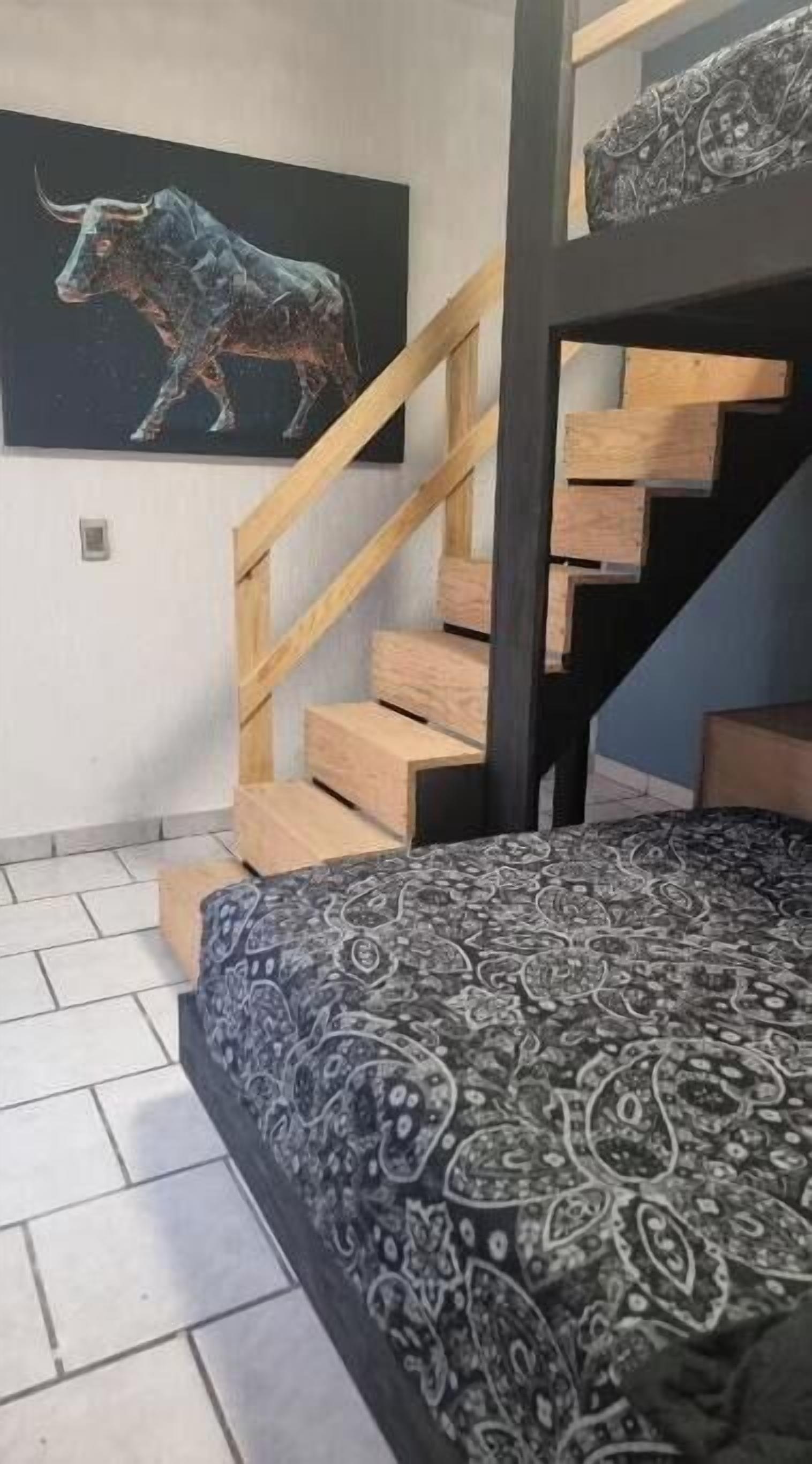 A bedroom with a patterned bedspread, a wooden staircase, and a bull painting on the wall.