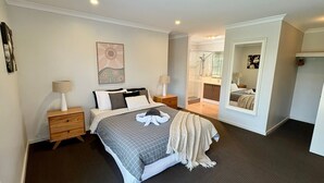 Ein Schlafzimmer mit Bett, Nachttischen, einem Spiegel und einem durchgegangenen Tür sichtbaren Badezimmer.