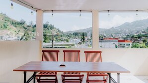Uma varanda com mesa e cadeiras de madeira, com vista para uma cidade e colinas.