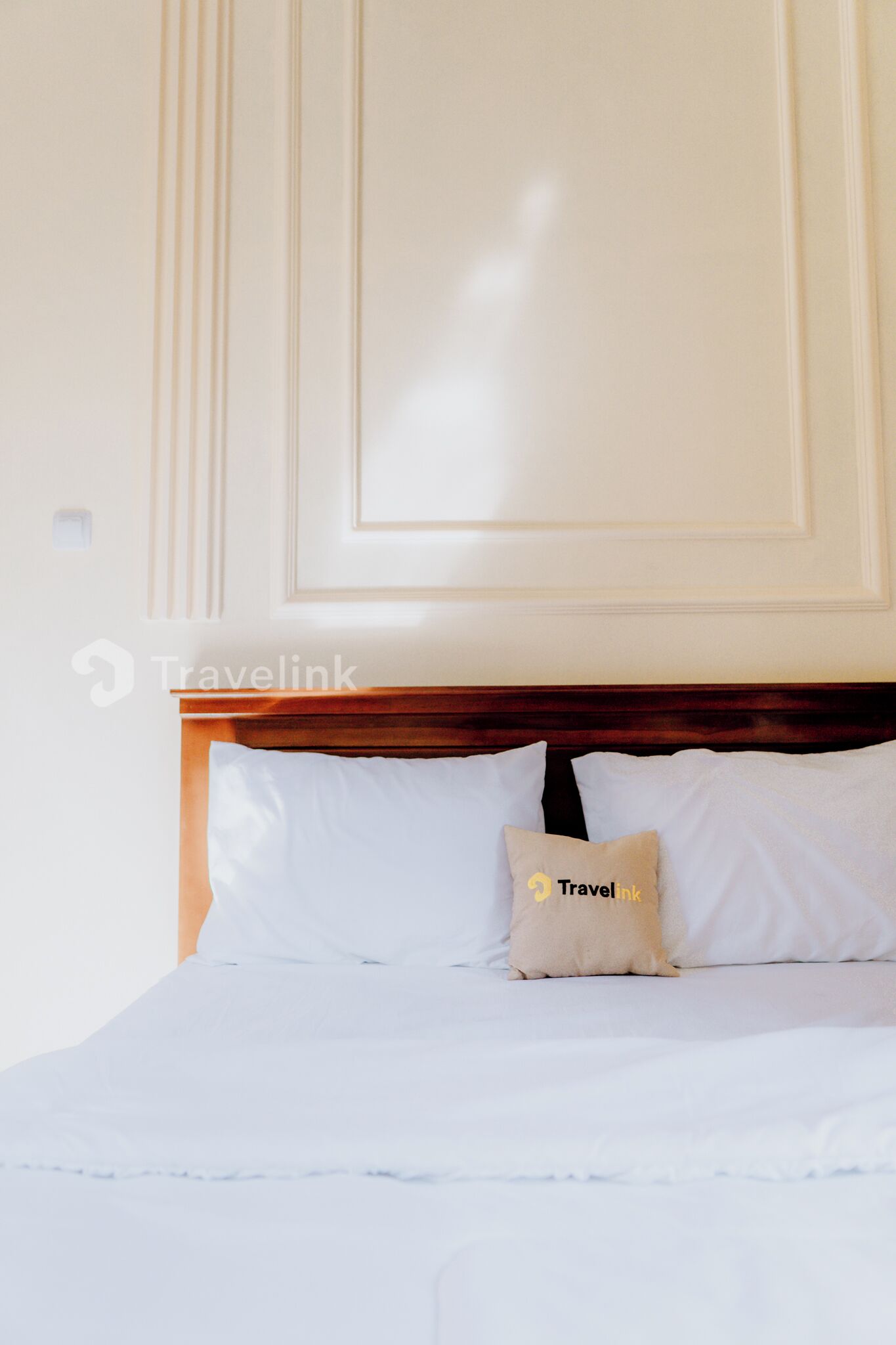 Quarto de hotel com cama bem arrumada, cabeceira de madeira e travesseiro com o logotipo TravelLink.