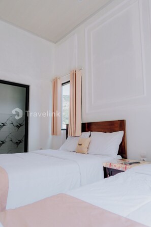 A hotel room with two beds, a wooden headboard, and a window with curtains. - Kurniawan By Travelink (Kejajar)