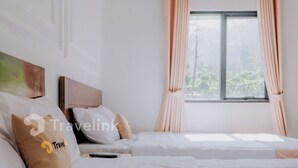 Quarto de hotel com duas camas, roupa de cama branca, uma janela com cortinas e um quadro na parede.