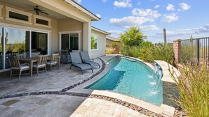 Uma piscina de borda curva, rodeada por um alpendre com cadeiras e uma mesa.