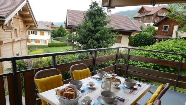 A balcony with a table set for breakfast, including bread, cups, and bowls.