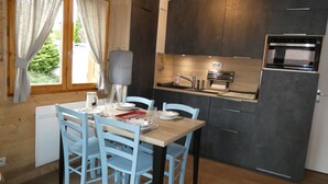 A modern kitchen with dark cabinets, a built-in oven, and a dining area with a wooden table and blue chairs.